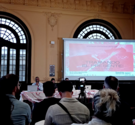 Salão principal do fórum de cultura da UFRJ lotado; no telão, a arte do simpósio Lavits com a tagline "Tramando o presente".